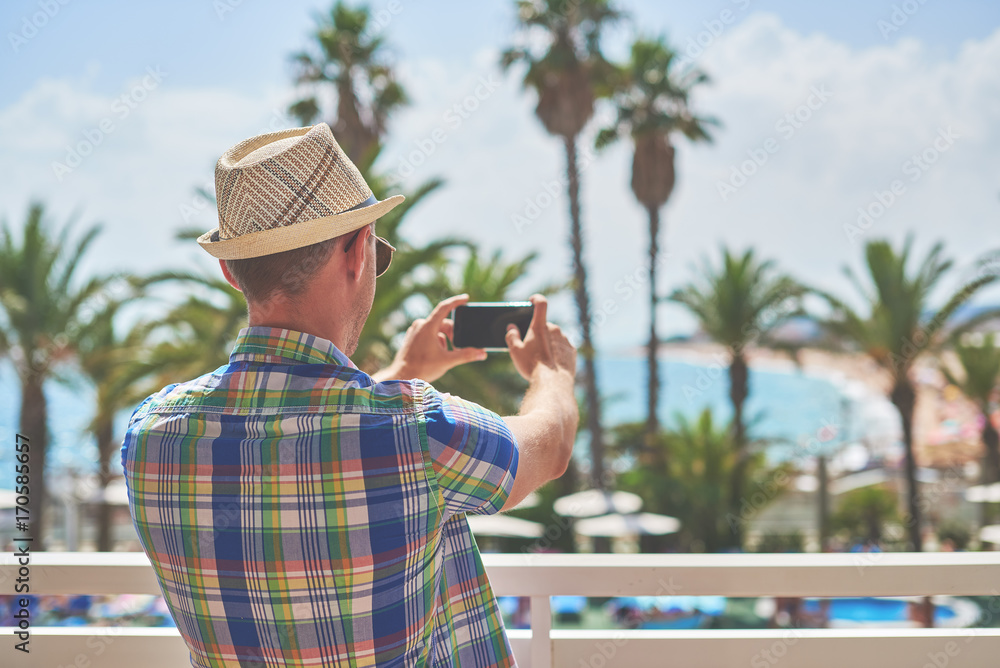 Man in sunhat making photo of amazing sea view with his smartphone. Santa Susanna. Cataluna. Spain.