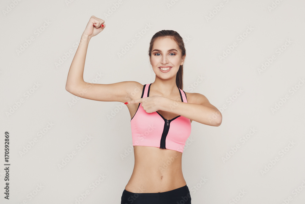 Fototapeta premium Smiling fitness woman shows her muscular hand