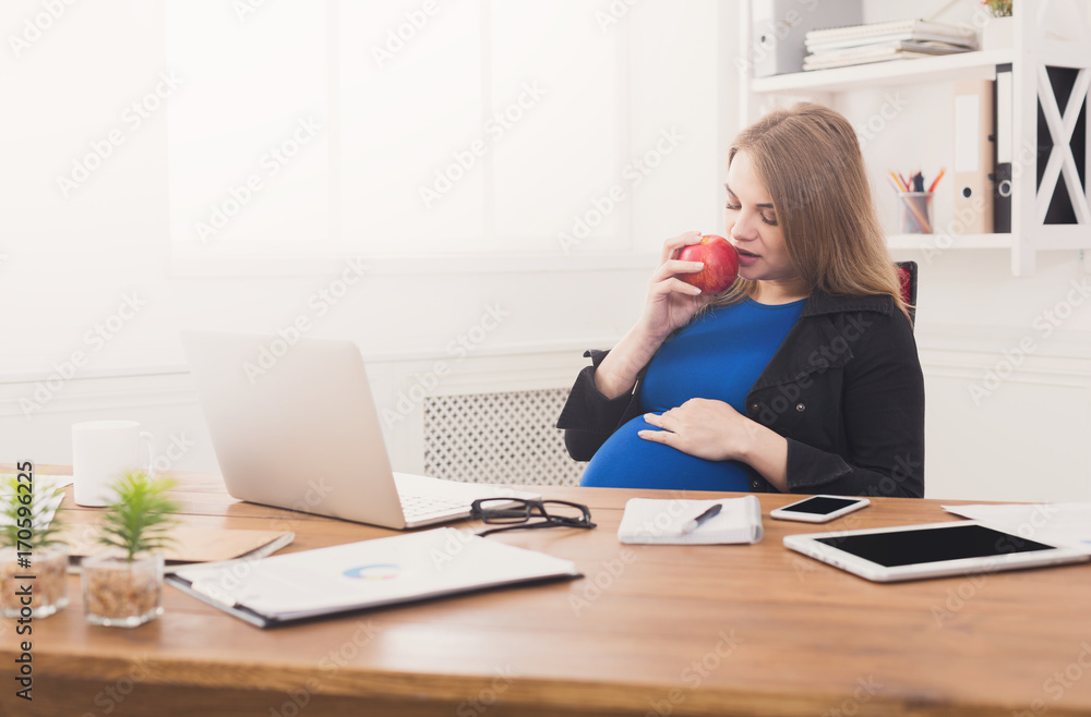 Pregnant woman eating apple in office copy space Pregnant woman eating apple in office copy space