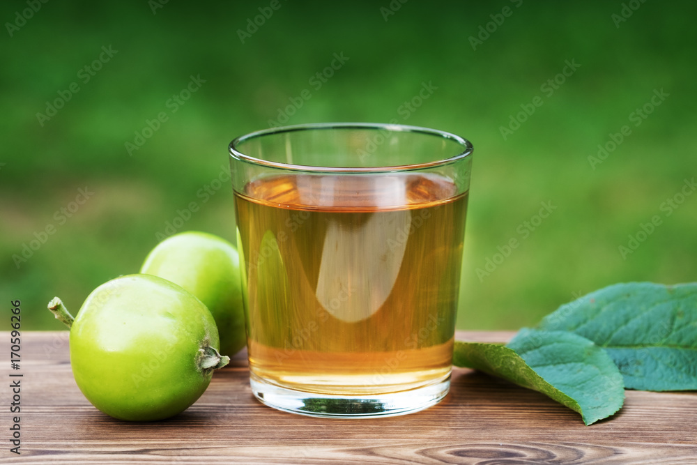 The juice of green apples in a glass on background of foliage The juice of green apples in a glass on background of foliage