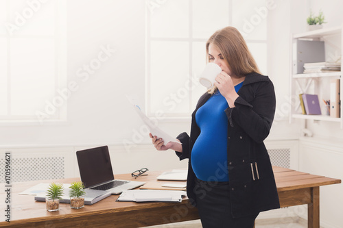 Pregnant business woman talking on phone with cup photo