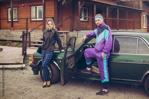 Guy and girl in clothes of the nineties, next to the old car