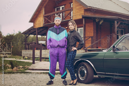 Guy and girl in clothes of the nineties, next to the old car