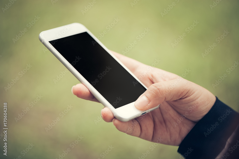 Close-up hand touch on phone mobile blank black screen outdoor lifestyle concept on blurry nature background - can be used mock up image. Vintage effect style pictures.