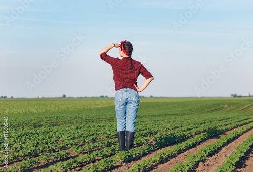 Rear view of female farmer standing in a soybean field and examining crop.