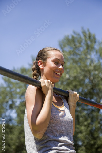 Young brunette woman doing pull-up on a sports horizontal bar at summer day