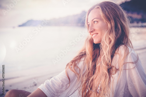 beautiful young woman with long blond hair sitting on the beach and admiring the sunset