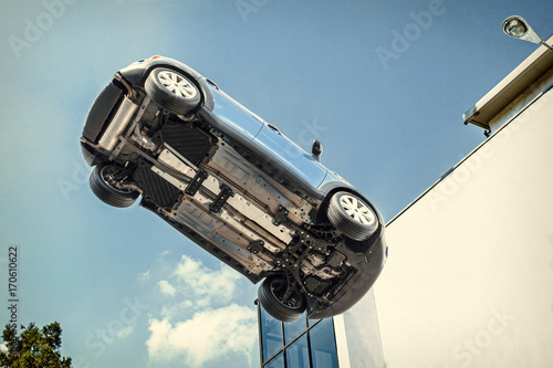 A car flying through the air (in the pale blue sky) with the underside including, wheels, engine and exhaust pipe visible.