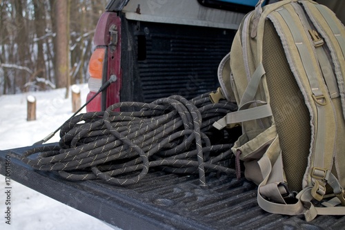 Khaki backpack and black rope in a trunk of a pickup truck. Winter time. Snow and sunlight. 
