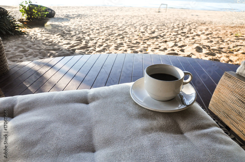 Close up coffee cup on wood table, coffee cup on the beach background, white cup of hot coffee on beach