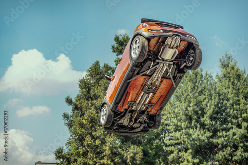 A car flying through the air (in the pale blue sky) with the underside including, wheels, engine and exhaust pipe visible.