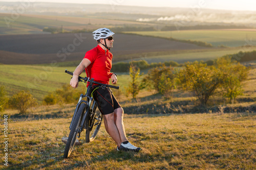 Biker tourist travel on mountain bike. Autumn landscape. Sportsman on bicycle in red jersey and white helmet