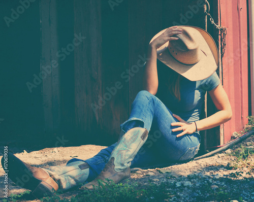Cowgirl showing western fashion while sitting, wearing cowboy hat and boots.   photo