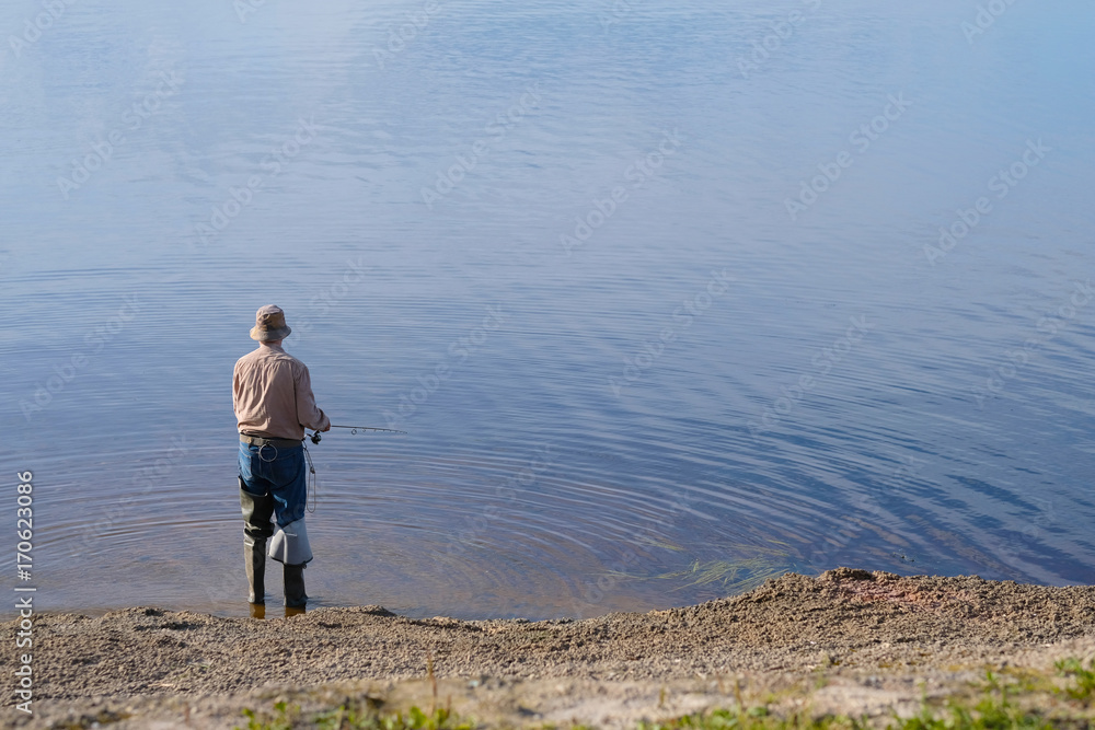 A lone man fishing while standing on the ground at the water's edge