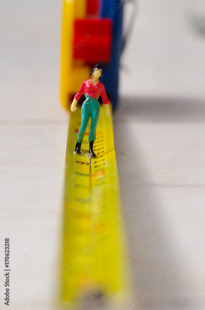 Miniature little people woman walking over a yellow tape measure isolated