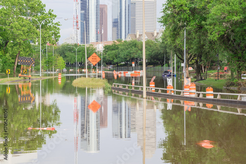 High water rising along Allen Parkway with road warning signs. Residential buildings and downtown Houston in background under cloudy sky. Heavy rains from tropical storm caused many floods. Swamp car photo