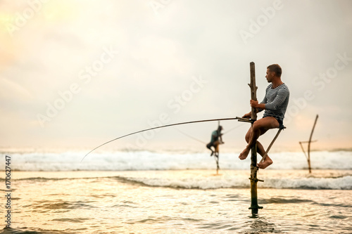 The European tourist is engaged in traditional fishing on poles in the Indian Ocean. Sri Lanka.
