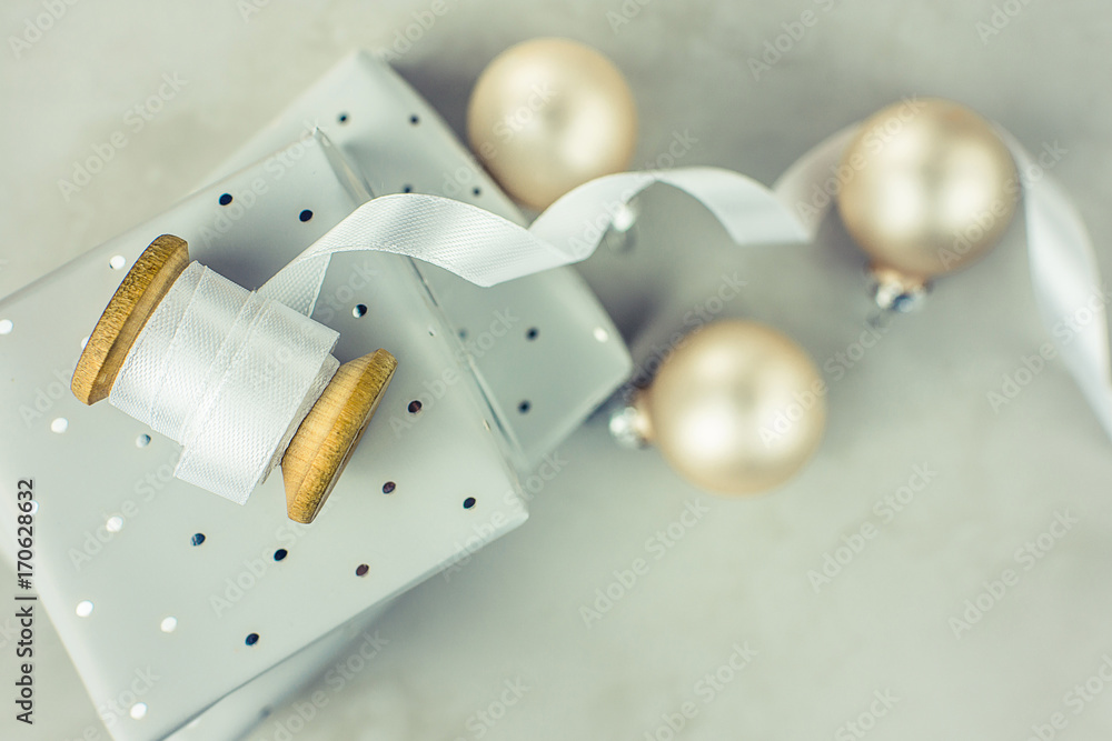 Stacked gift boxes wrapped in silver paper with polka dots pattern. Wooden spool with white curled silk ribbon, Christmas baubles on stone marble background. Top view, copy space. Stacked gift boxes wrapped in silver paper with polka dots pattern. Wooden spool with white curled silk ribbon, Christmas baubles on stone marble background. Top view, copy space.