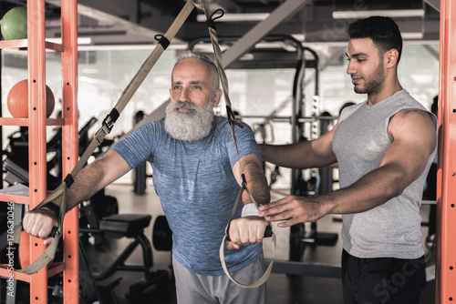 Confident senior male enjoying workout with trainer in athletic center
