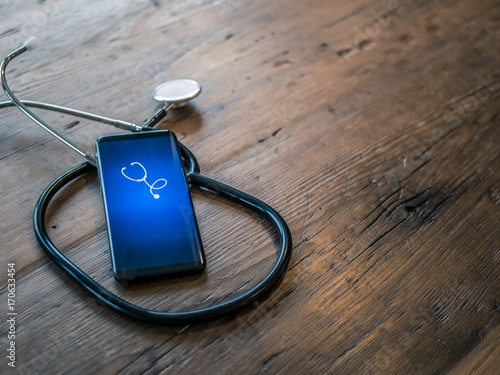 Mobile phone with healthcare app on wood table with stethoscope photo