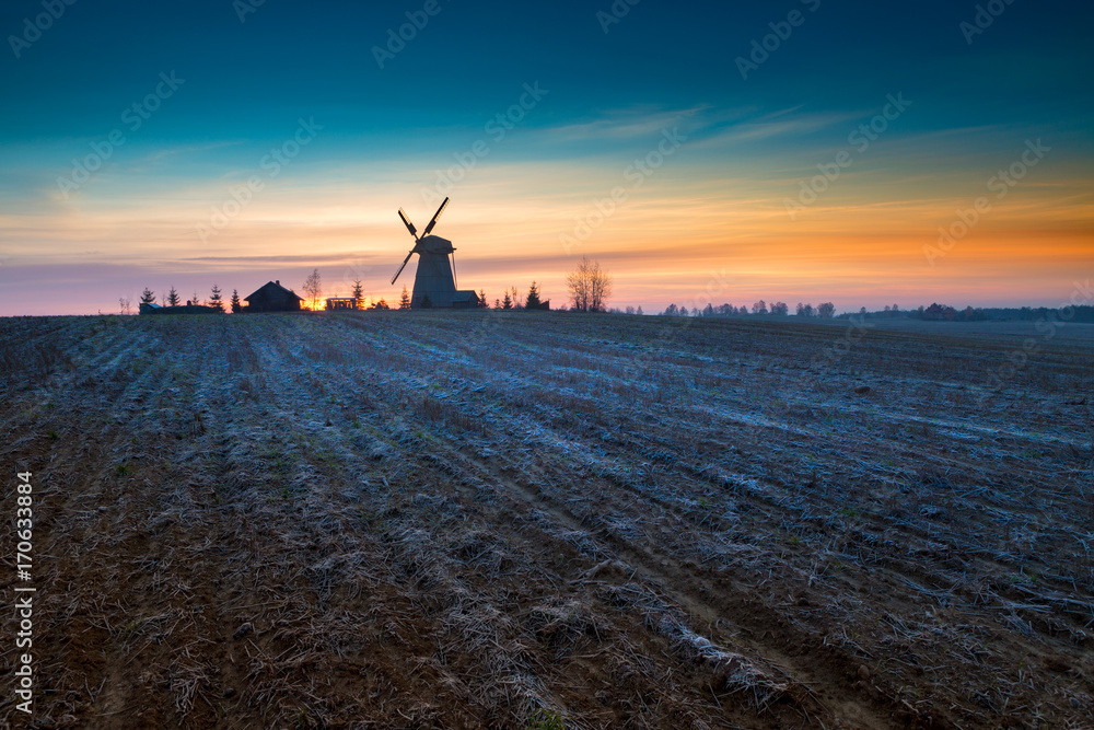 Frosted autumn sunrise behind wooden windmill in Dudutki village, Minsk Region, Belarus