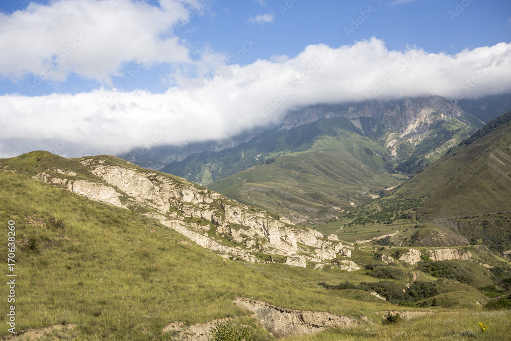 Горный пейзаж. Красивый вид на живописное ущелье, панорама горной местности, белые облака на синем небе. Природа и горы Северного Кавказа