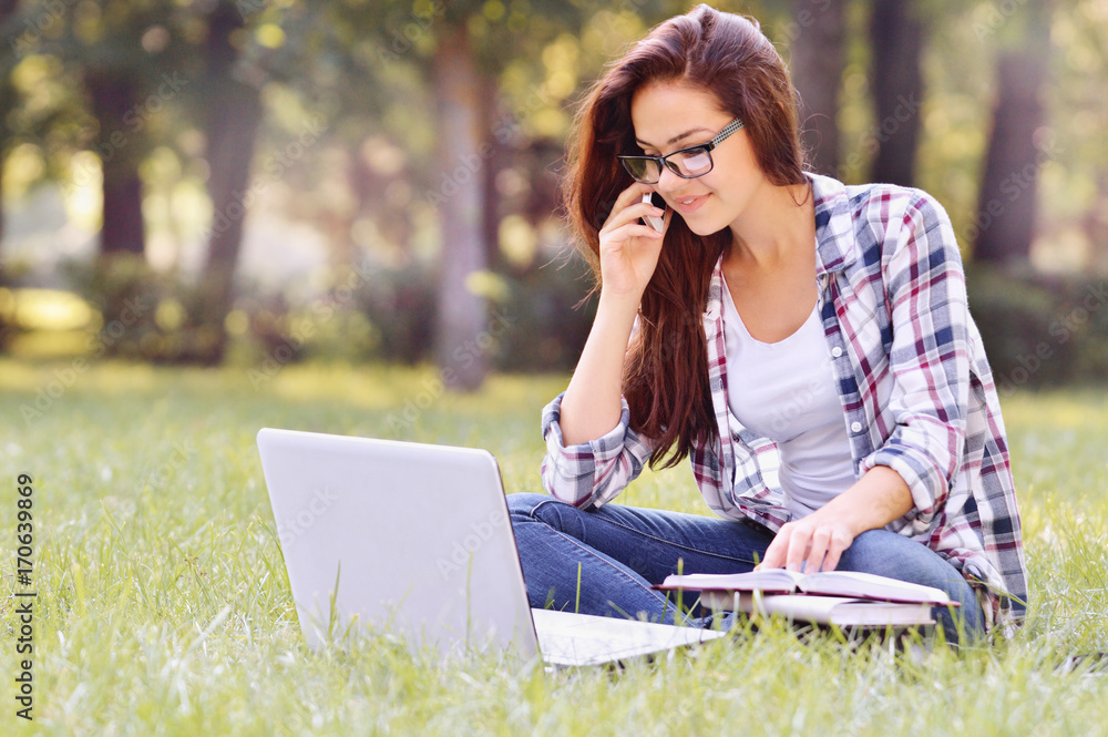 Student girl working on laptop, sitting on grass in park Student girl working on laptop, sitting on grass in park