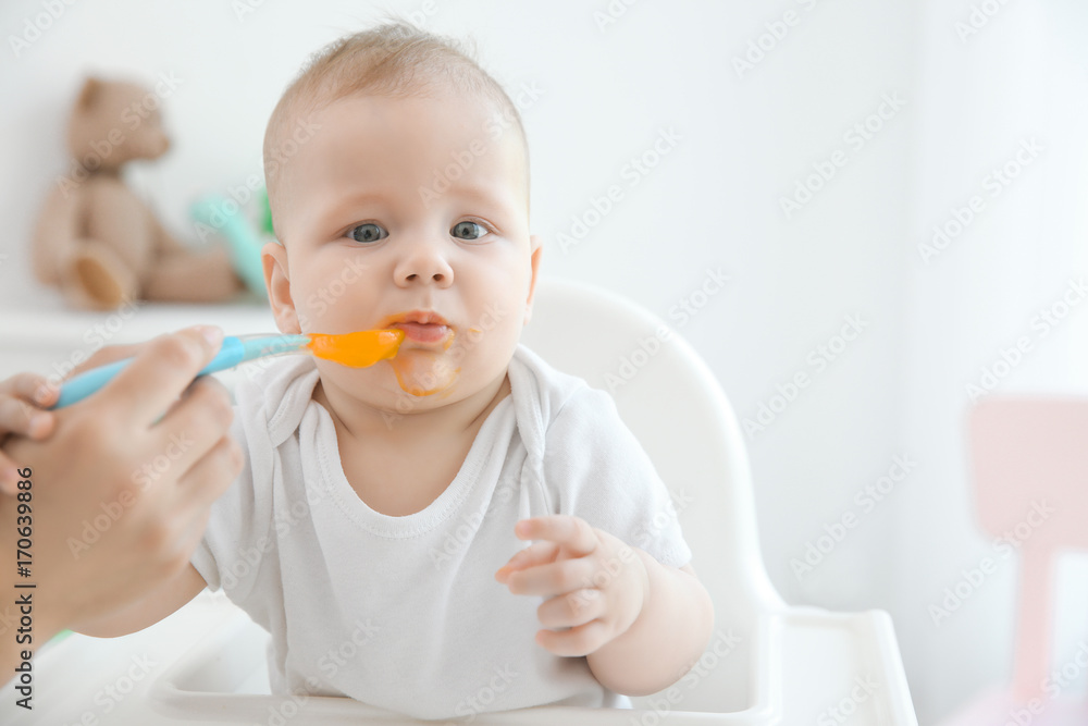 Mother feeding baby with spoon indoors Mother feeding baby with spoon indoors