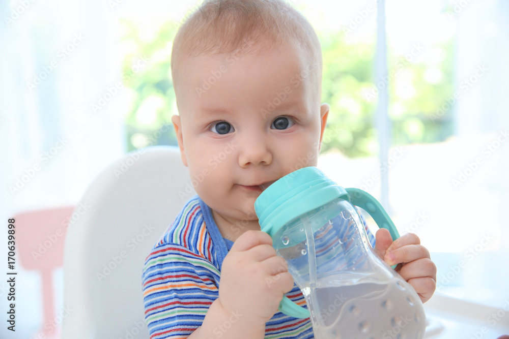 Cute baby drinking water from plastic bottle indoors Stock Photo