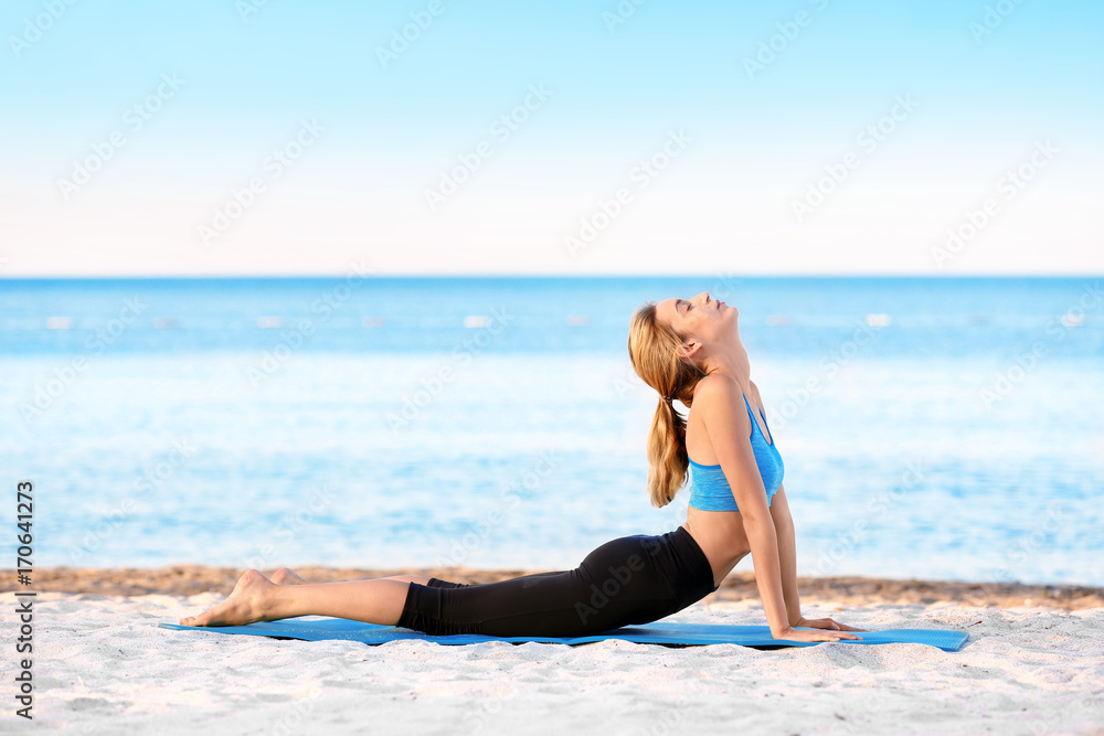 Beautiful young woman practicing yoga on sea beach