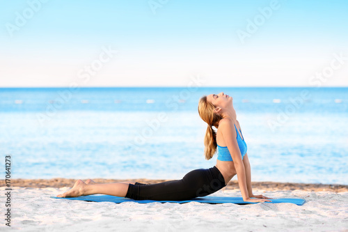 Beautiful young woman practicing yoga on sea beach © Africa Studio