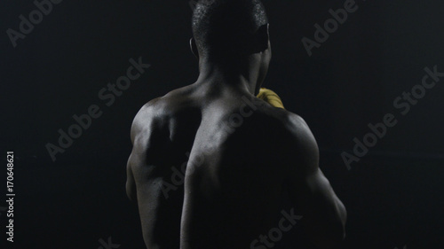 Rear view of muscular man boxing on black background. Afro american young male boxer practicing shadow boxing. Boxer in yellow Boxing gloves