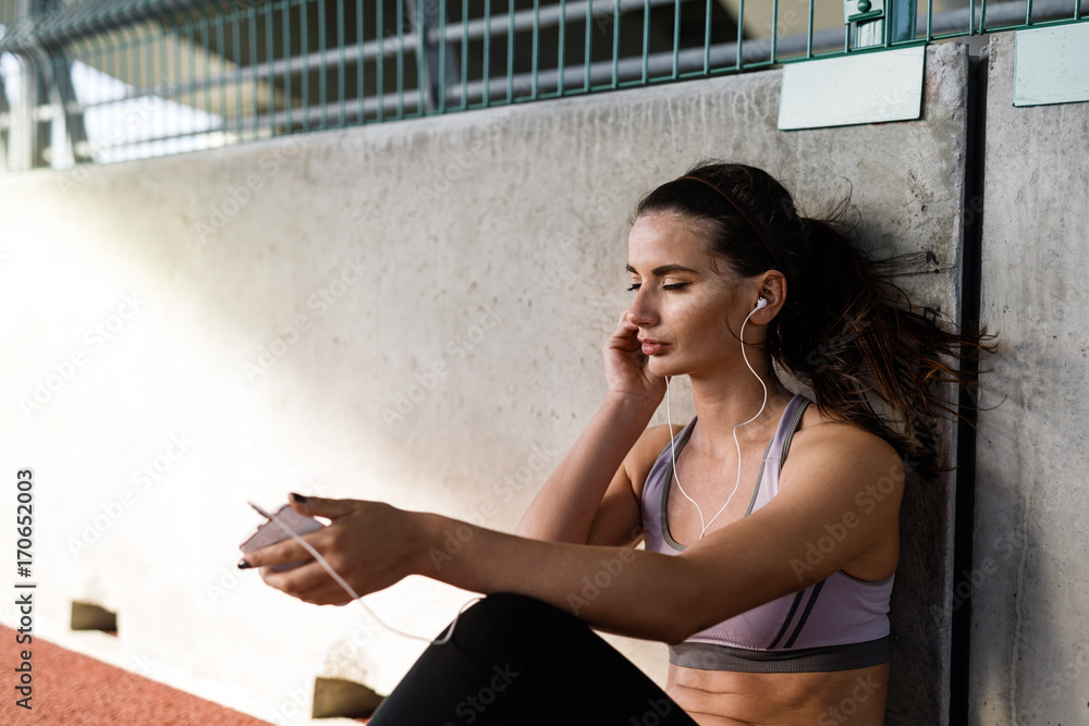 Young sportswoman relaxing after exercises, sitting on footpath