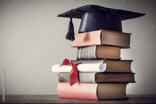 Graduation hat and diploma with book on table