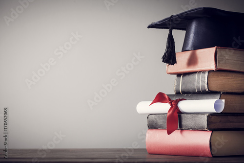 Graduation hat and diploma with book on table photo