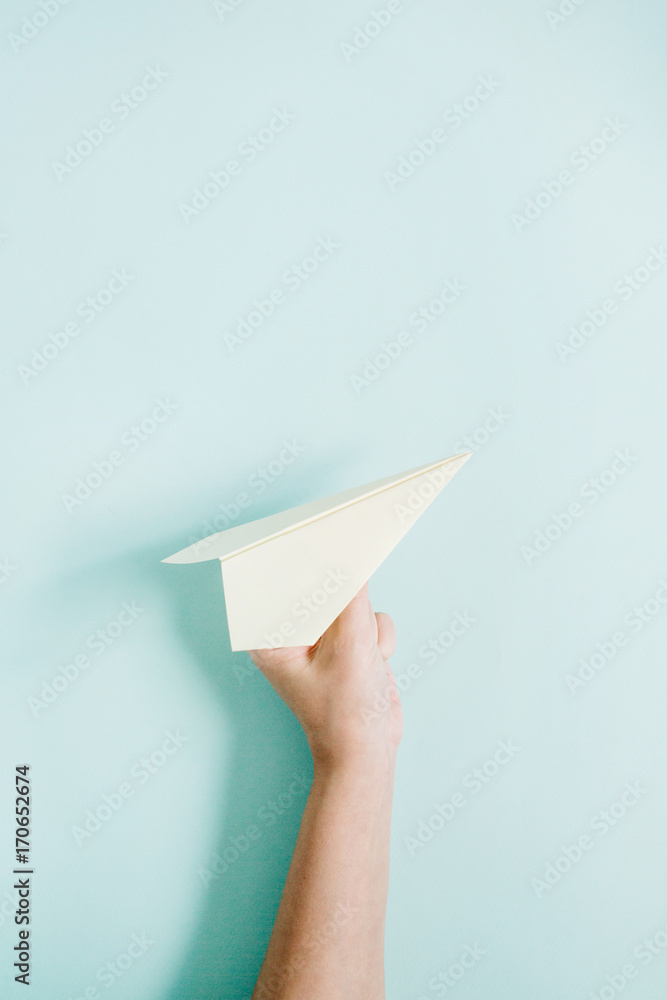 Obraz premium Women hand holding white paper plane on pale blue background. Flat lay, top view.