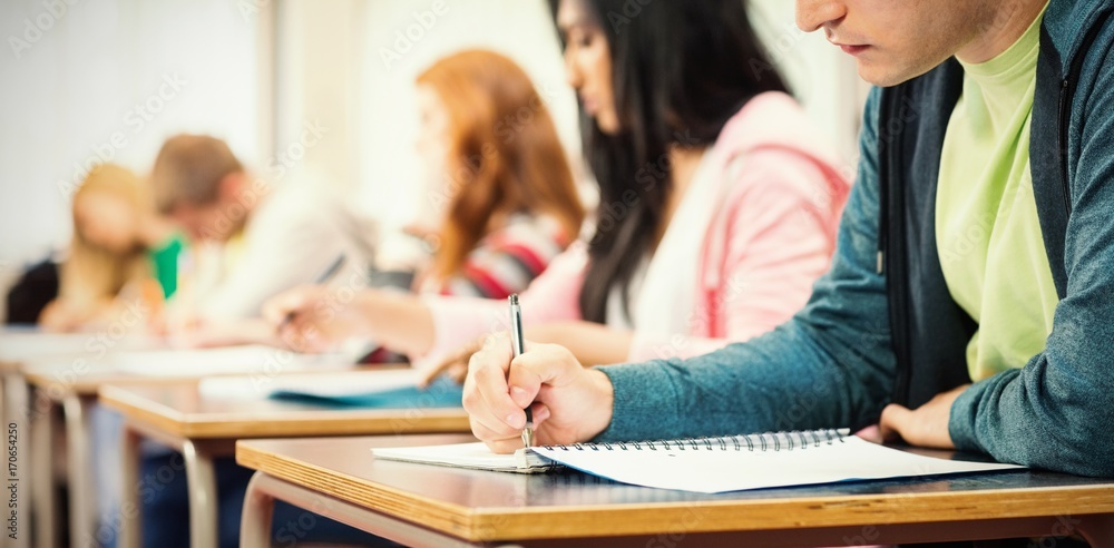 Young students writing notes in classroom - obrazy, fototapety, plakaty 