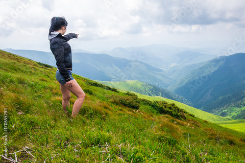 Landscape, travel, tourism. A girl stands and shows her hand in the mountains. Horizontal frame