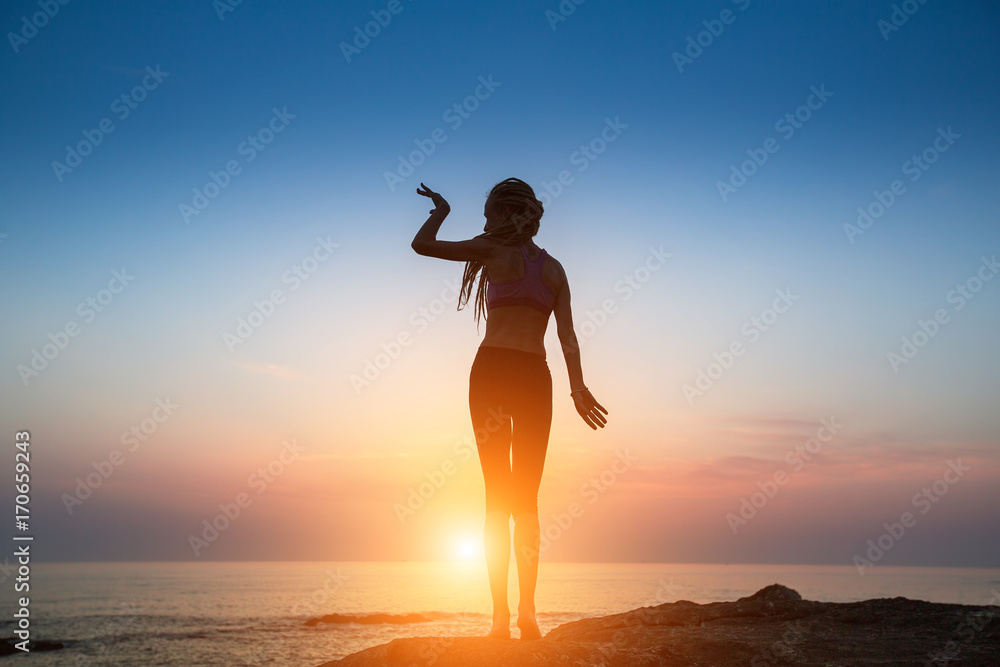 Silhouette flexible girl moves in a dance on the shore of the sea during twilight.