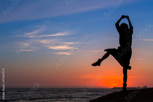 Silhouette of flexible girl on  sea coast during sunset.