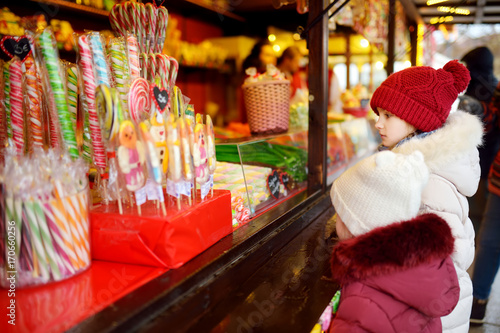 Cute little sisters choosing sweets on traditional Christmas market on chilly winter day.