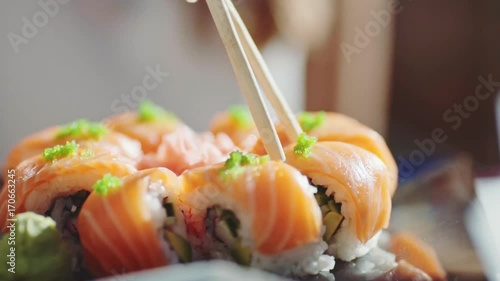 Woman Hand With Chopsticks Taking Sushi. 4K Close Up. Girl eating sushi rolls with salmon on outdoor terrace of Japanese restaurant.  