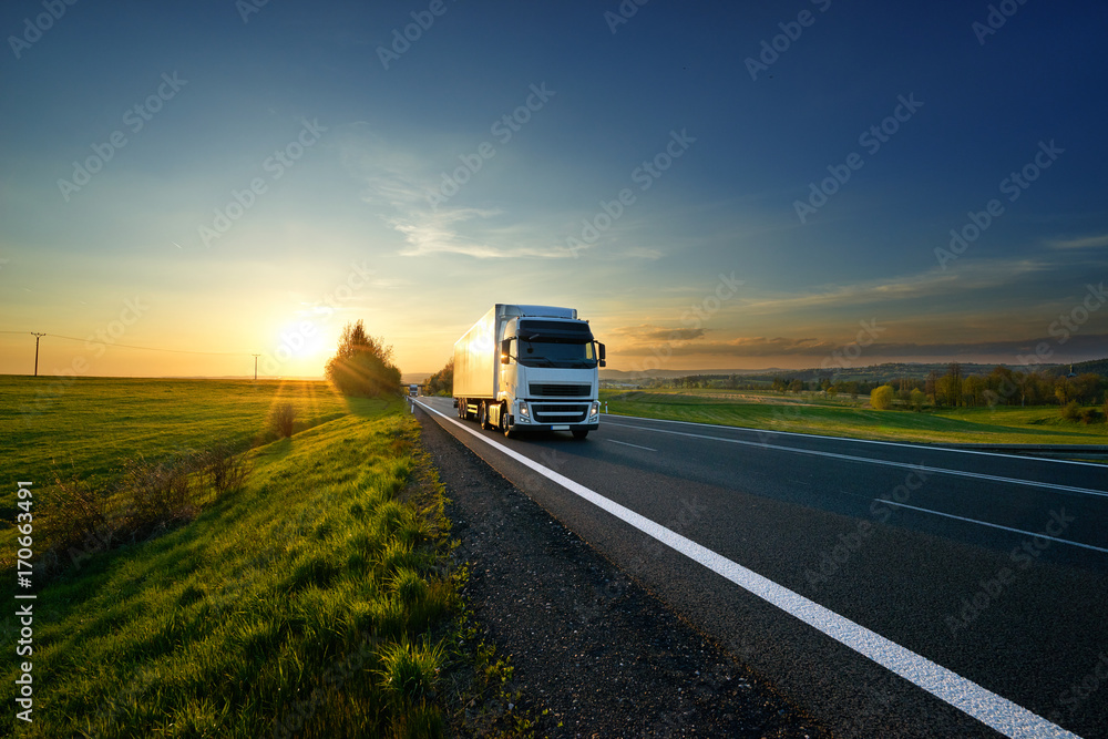 White truck driving on the asphalt road in rural landscape at sunset