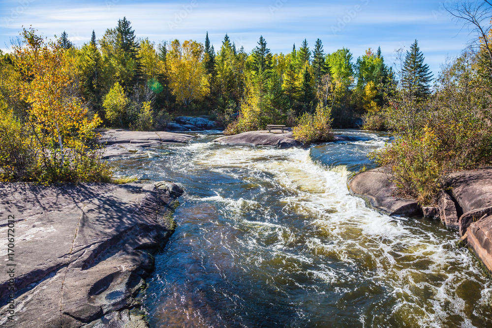 Fototapeta premium Old Pinawa Dam Provincial Heritage Park. Warm autumn day. Foam water rapids on the smooth stones of the Winnipeg River. The concept of ecological and adventure tourism
