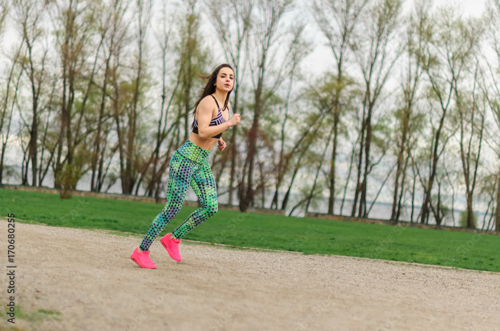 Girl beautiful brunette. Athletic body , pumped muscles. Bright colors , green ,pink .running in the Park .