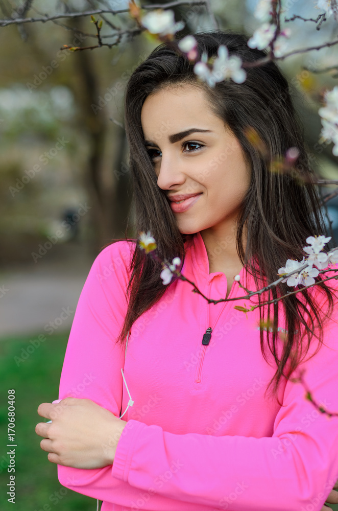 Naklejka premium Girl beautiful brunette. A sports body, having pumped up muscles. Bright colors, green, pink. Spring, trees in bloom. She does exercises.