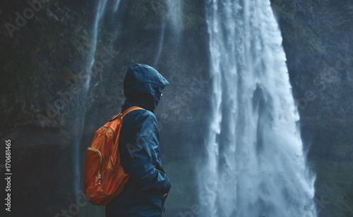 Fotografi Girl in waterproof clothing stands under the Seljalandsfoss waterfall in Iceland