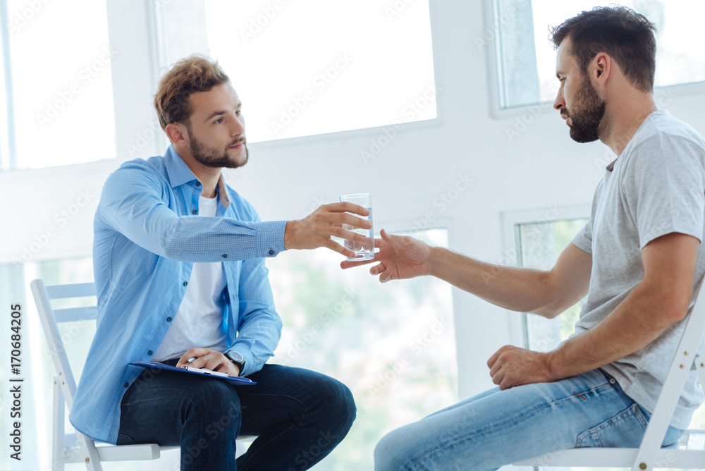 Obraz premium Nice helpful psychologist giving water to his patient