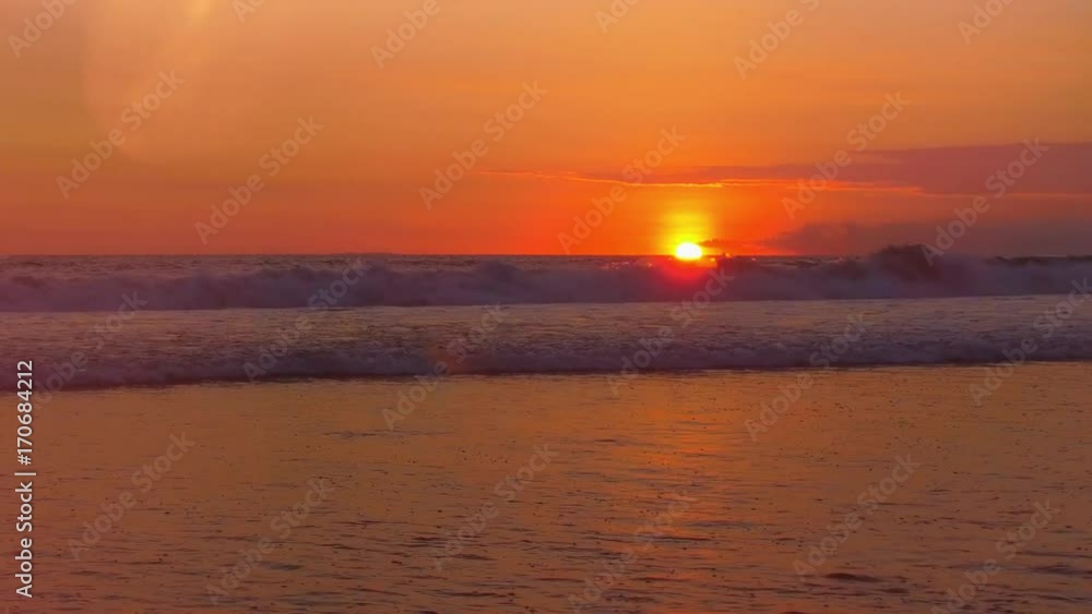 LENS FLARE: Big curly waves breaking and rolling towards the sea shore at gorgeous red sunset on tranquil summer evening in dreamy Bali island, Indonesia. Rippling sea splashing at golden light sunset LENS FLARE: Big curly waves breaking and rolling towards the sea shore at gorgeous red sunset on tranquil summer evening in dreamy Bali island, Indonesia. Rippling sea splashing at golden light sunset