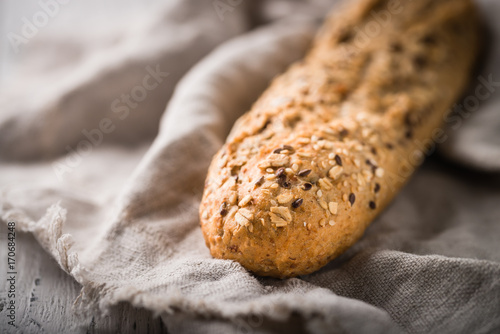 Fresh, healthy whole grain rye loaf on cloth and rustic wooden table, baguette close up. Bakery and grocery concept